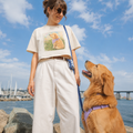 Ivory boxy t-shirt printed with a Golden Retriever puppy in a lavender bandana sitting in a grassland